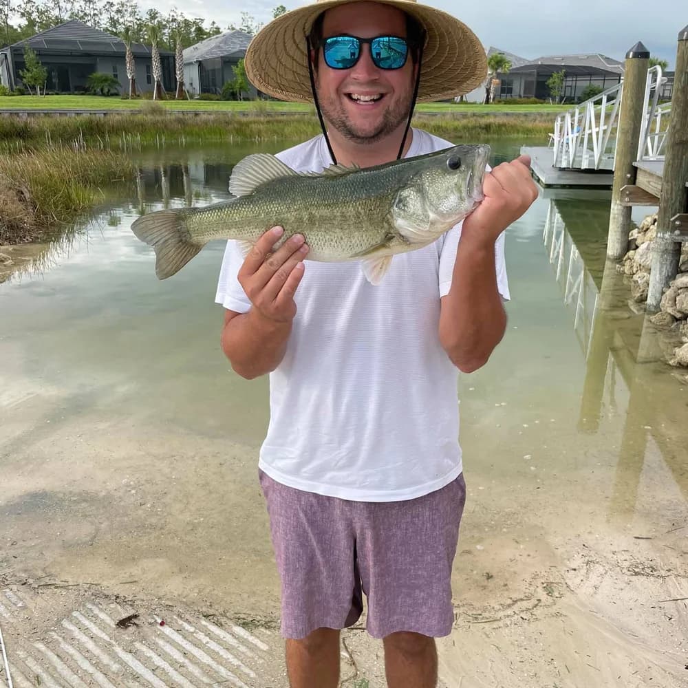 A smiling man holding a bass beside a WildBlue neighborhood dock