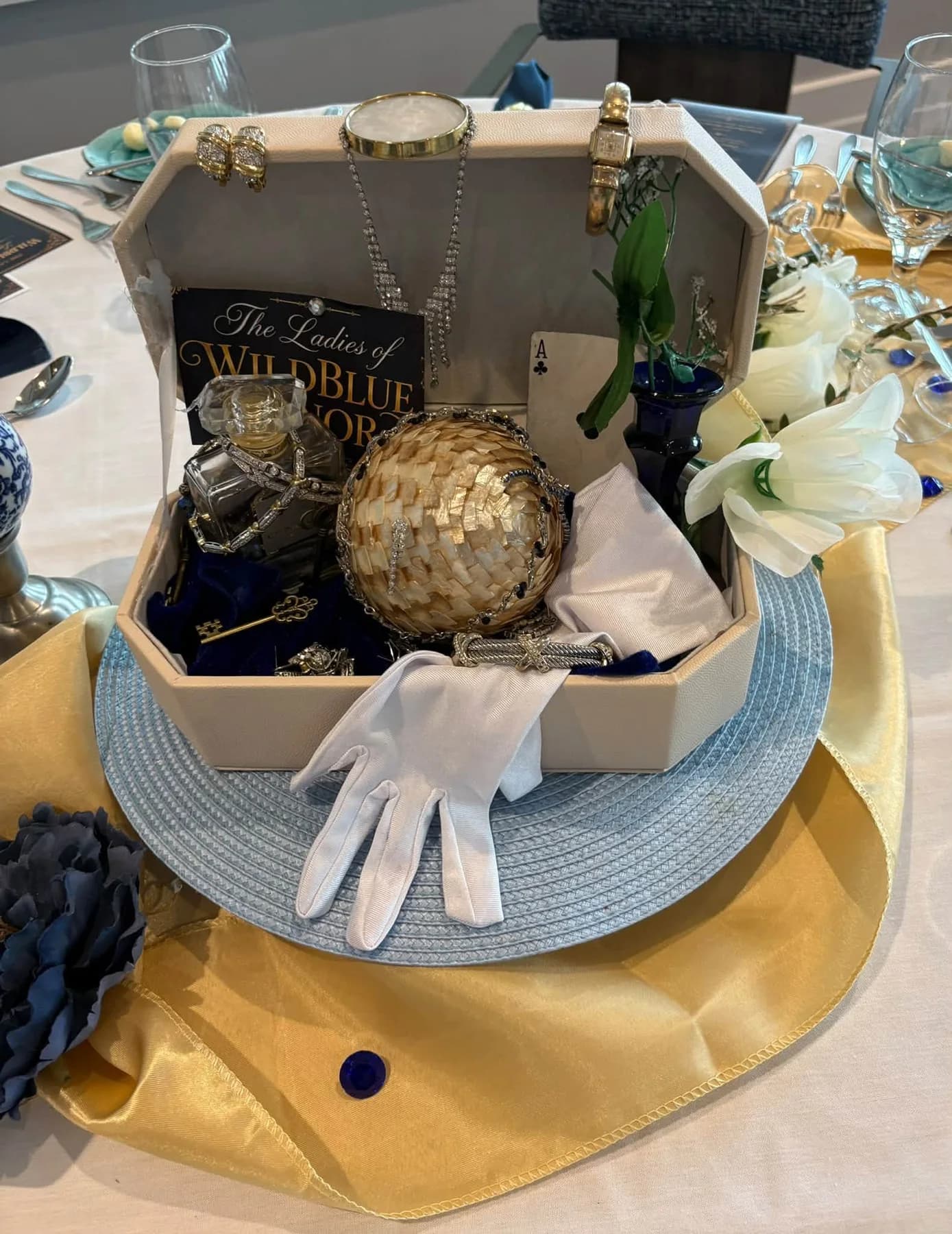 A jewelry-box centerpiece with white gloves, flowers, and sparkling accessories
