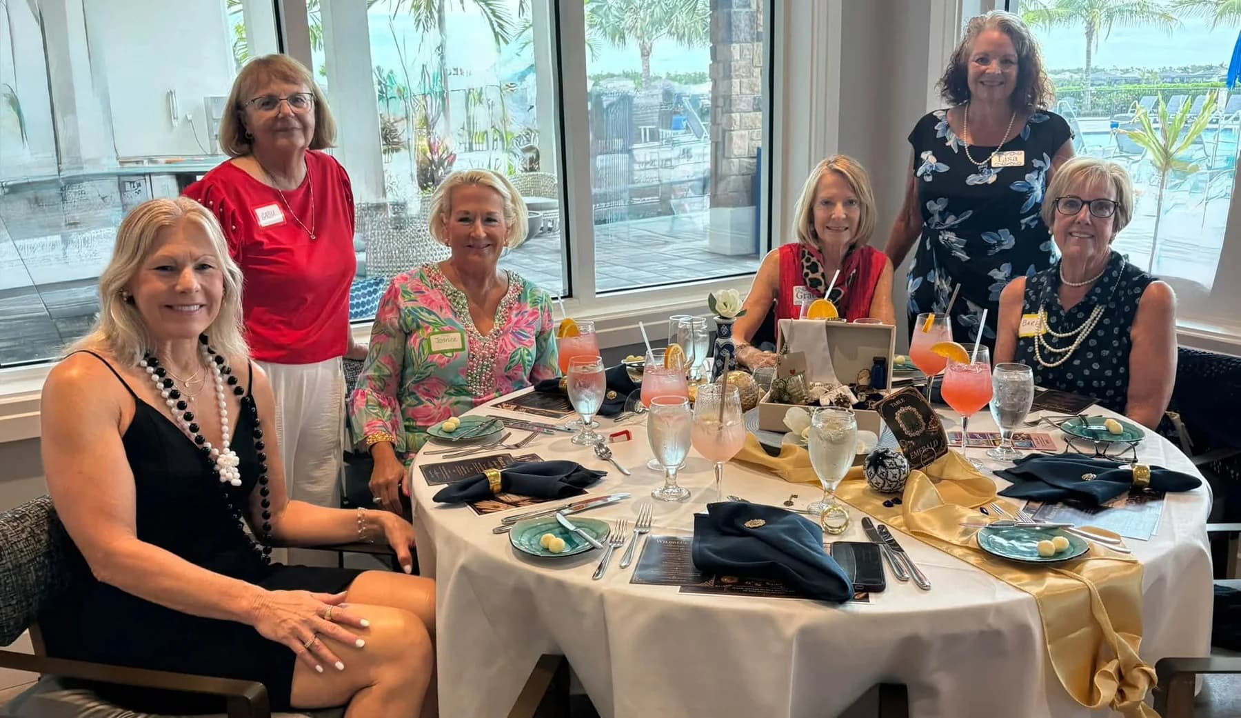 Friends gathered around a luncheon table beside the dining room windows