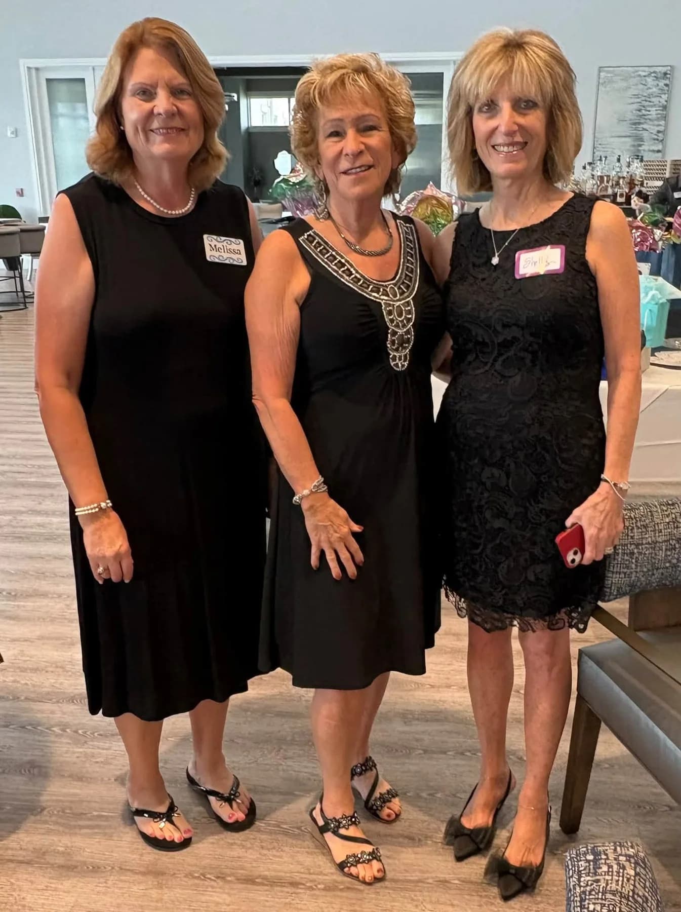 Three friends in black dresses posing together at the luncheon