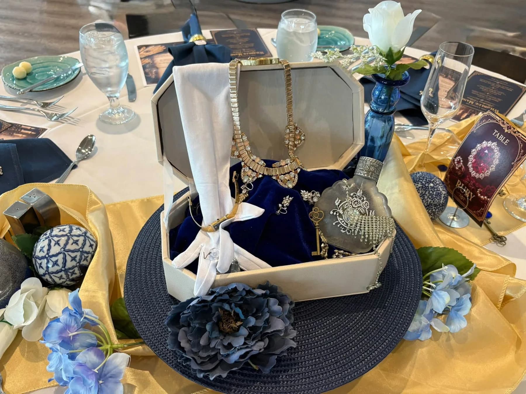 A centerpiece with a navy hat, pearls, white gloves, and blue flowers