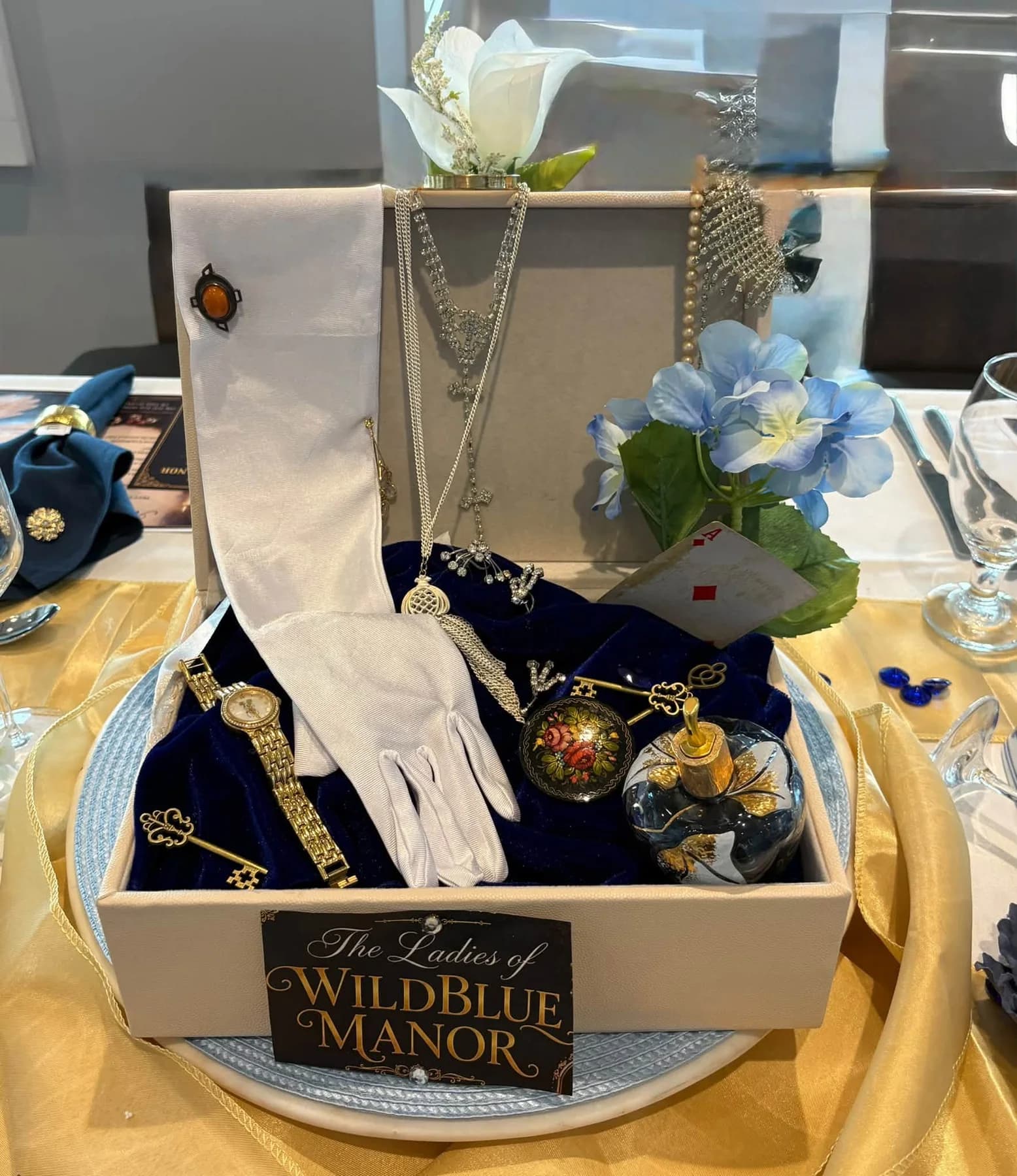 A WildBlue Manor centerpiece with pearls, gloves, and blue flowers