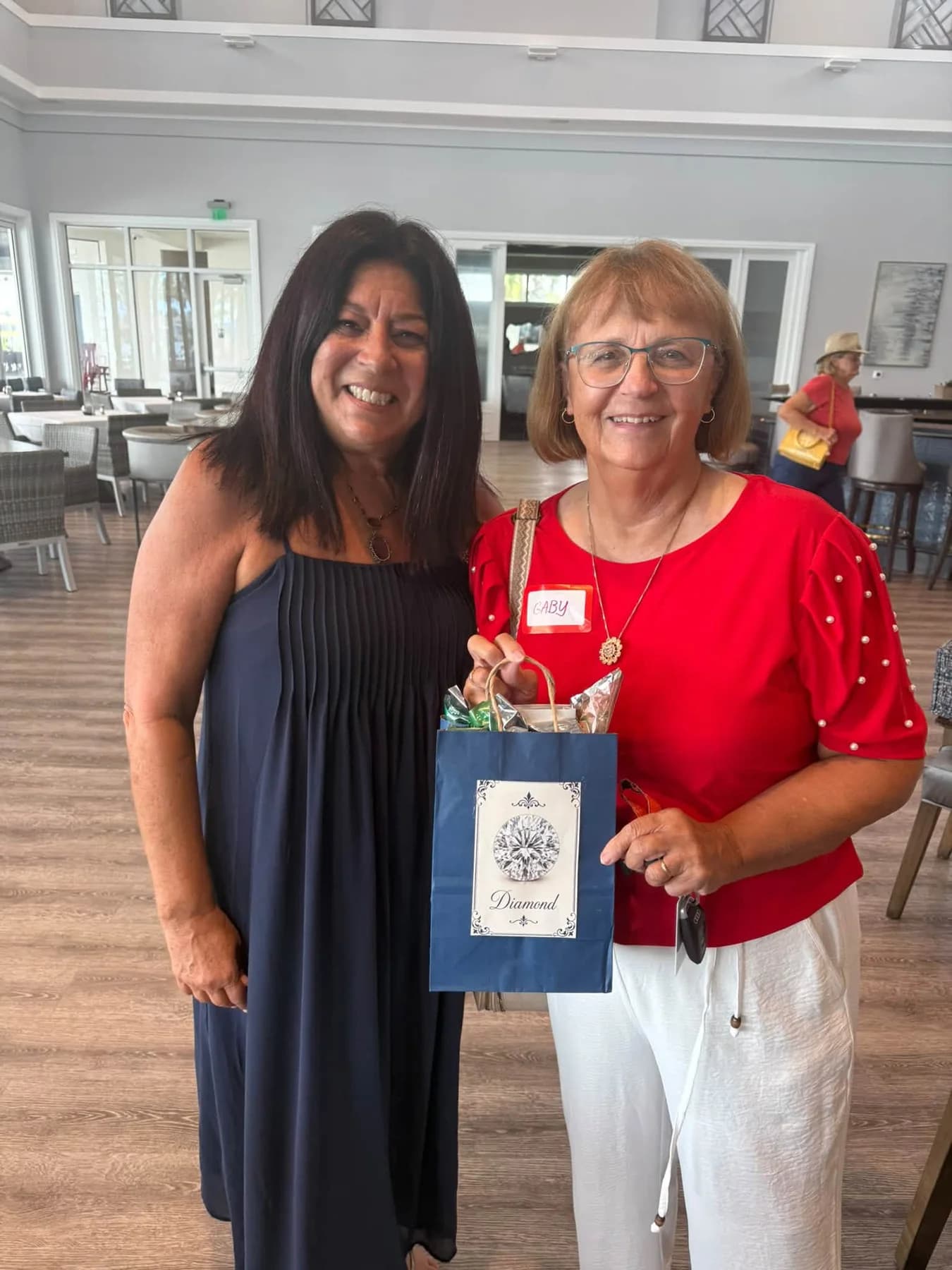 Two luncheon guests posing with a navy gift bag