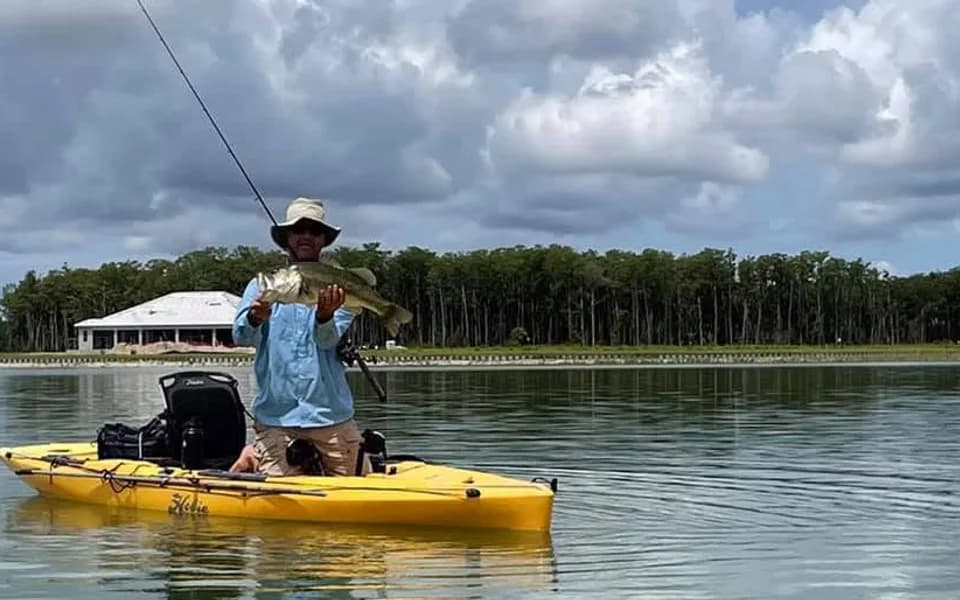A WildBlue resident holding a fish from a yellow kayak on the lake