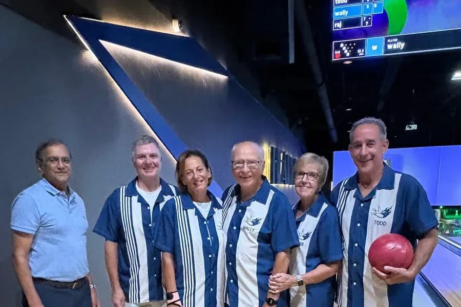 A mixed group of six WildBlue residents smiling together at a bowling alley